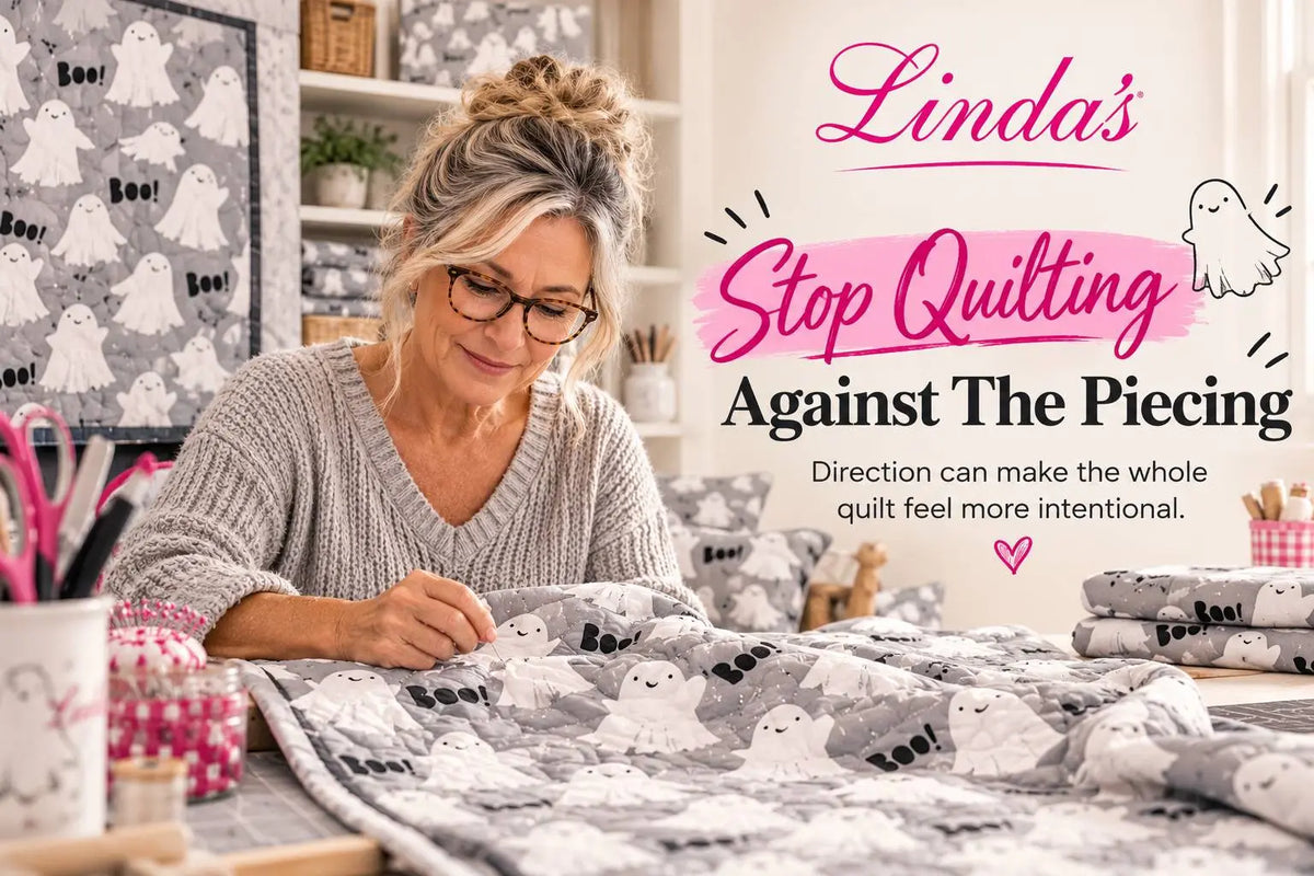 Wide, eye-level view of a woman wearing glasses and a gray knit sweater sewing a gray-and-white quilt patterned with ghosts and the word “Boo!” in a b...