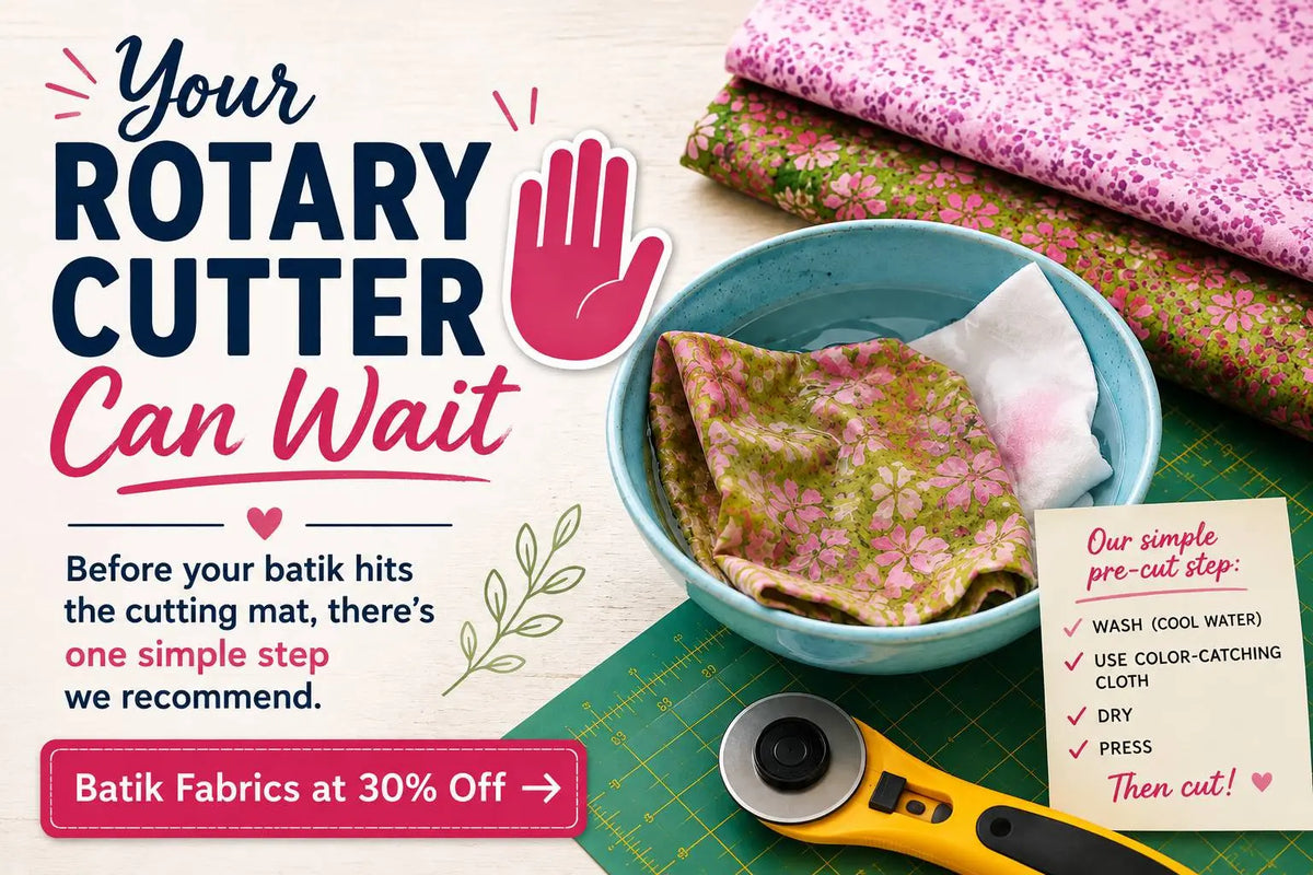 A flat lay with pink floral batik fabric, a blue bowl of water with fabric soaking, and a yellow rotary cutter on a green cutting mat